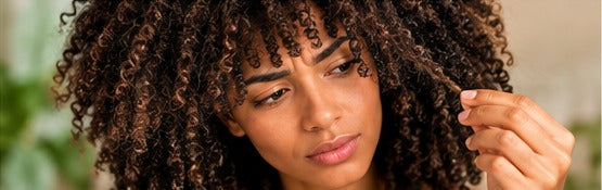 Femme examinant ses boucles naturelles, illustration sur frisottis et cheveux secs